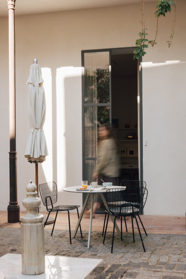 Una persona se mueve por el patio interior del hotel boutique Plácido y Grata de Sevilla, rodeada de mobiliario y una fuente típica
